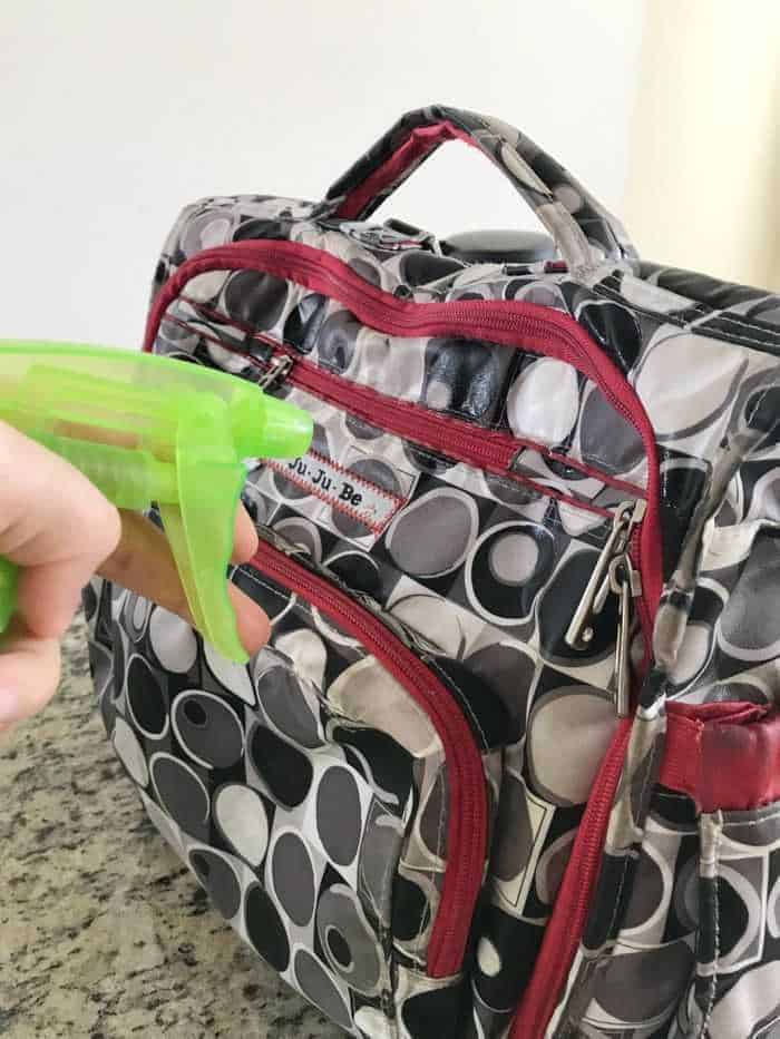 A woman spraying a JuJuBe bag clean