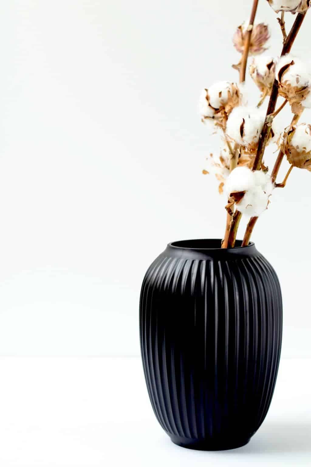 A minimalist black vase with cotton inside of it