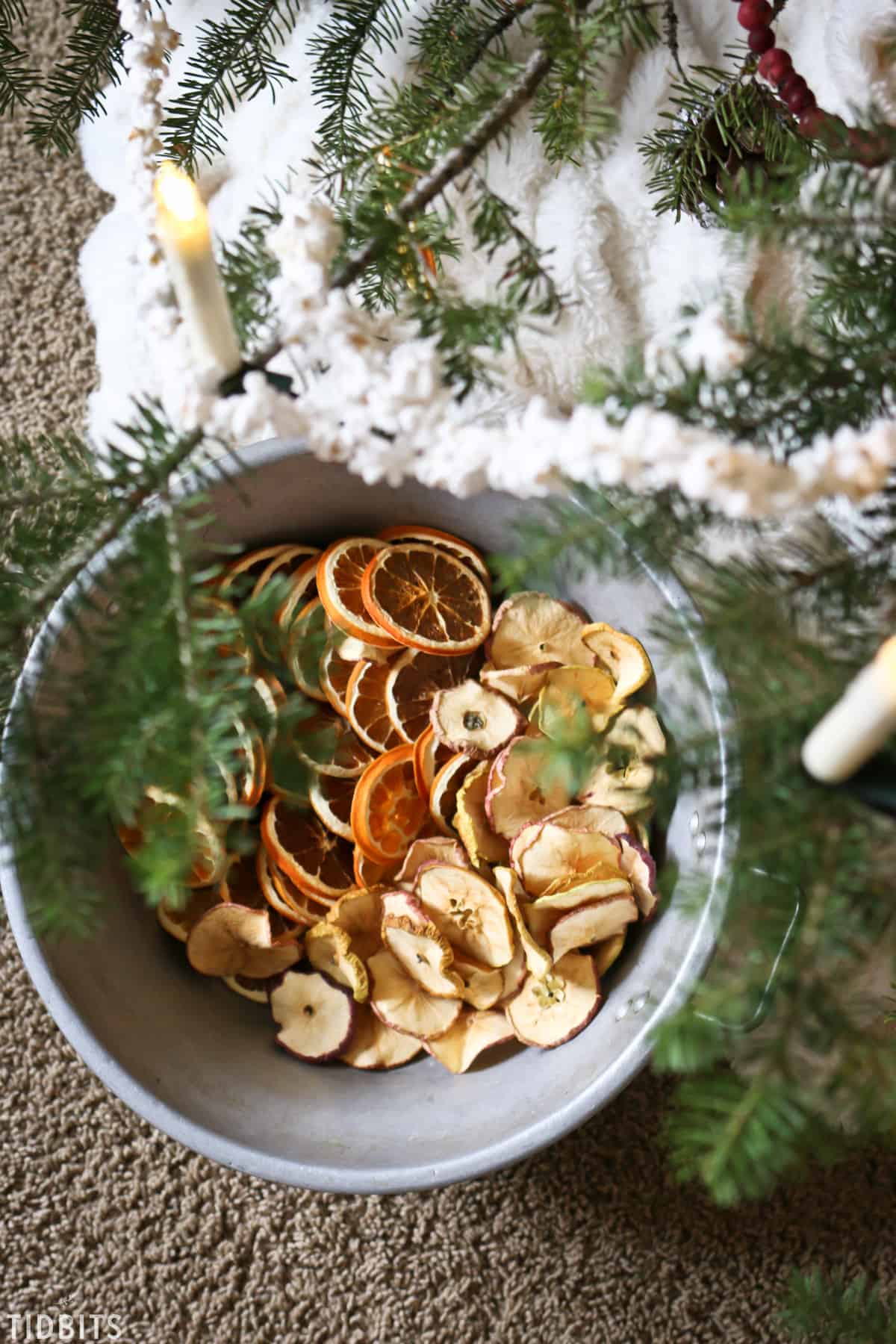 A bowl of natural orange and apple decorations being hung on a Christmas tree.