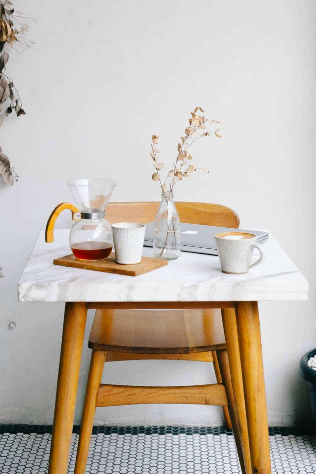 A minimalist marble table with pour over coffee and a laptop on top