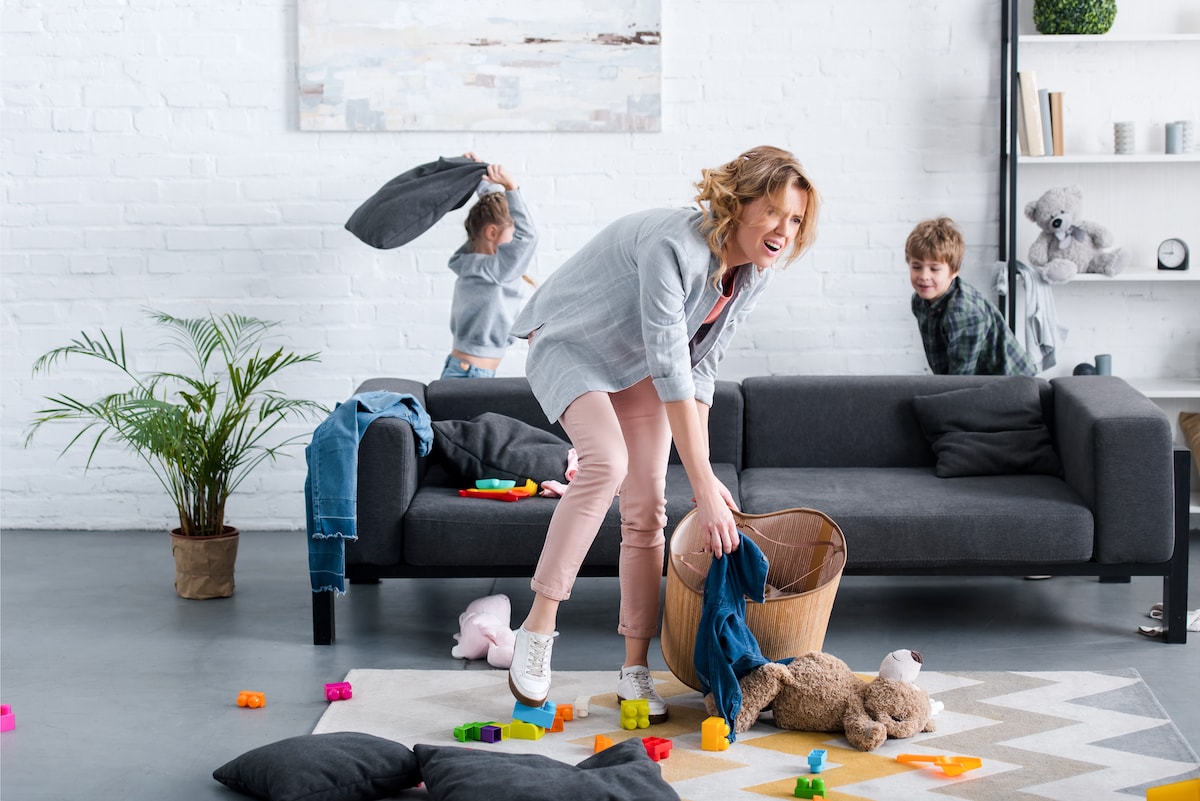An overwhelmed mom struggling to declutter with her kids jumping around like crazy