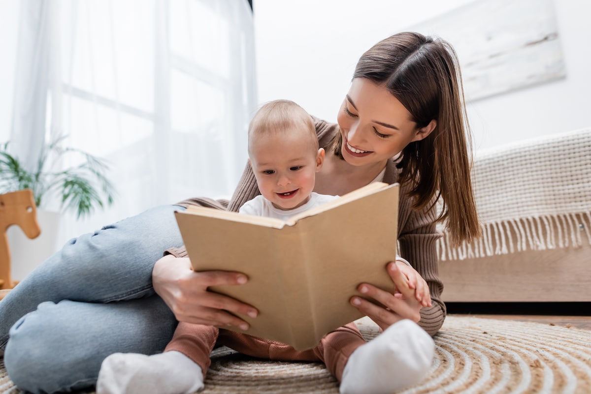 Happy women and baby enjoying reading a book on the bright, clutter-free, living room floor