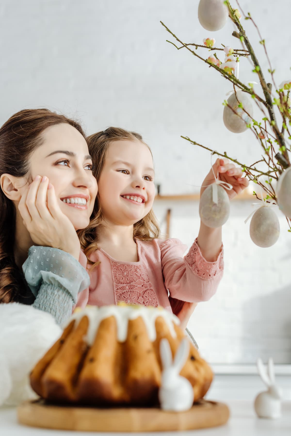 A happy mom and daughter hanging Easter eggs as part of a family ritual