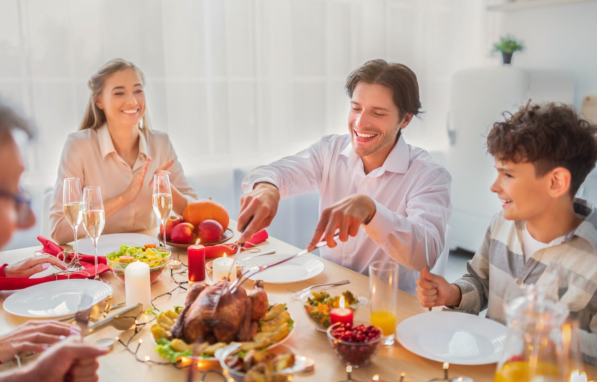 A happy family laughing as they share the family ritual of carving the turkey for holiday dinner.