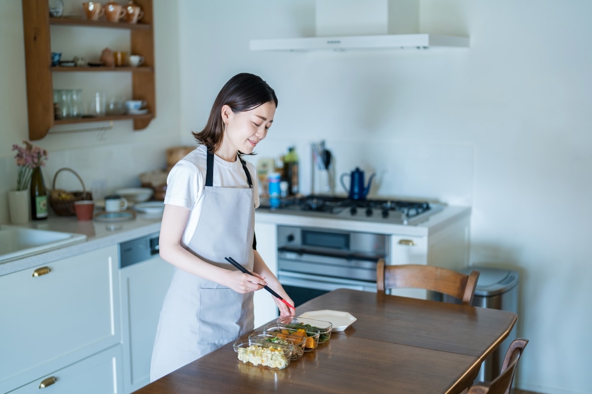A minimalist person smiling while preparing leftover food in her kitchen.