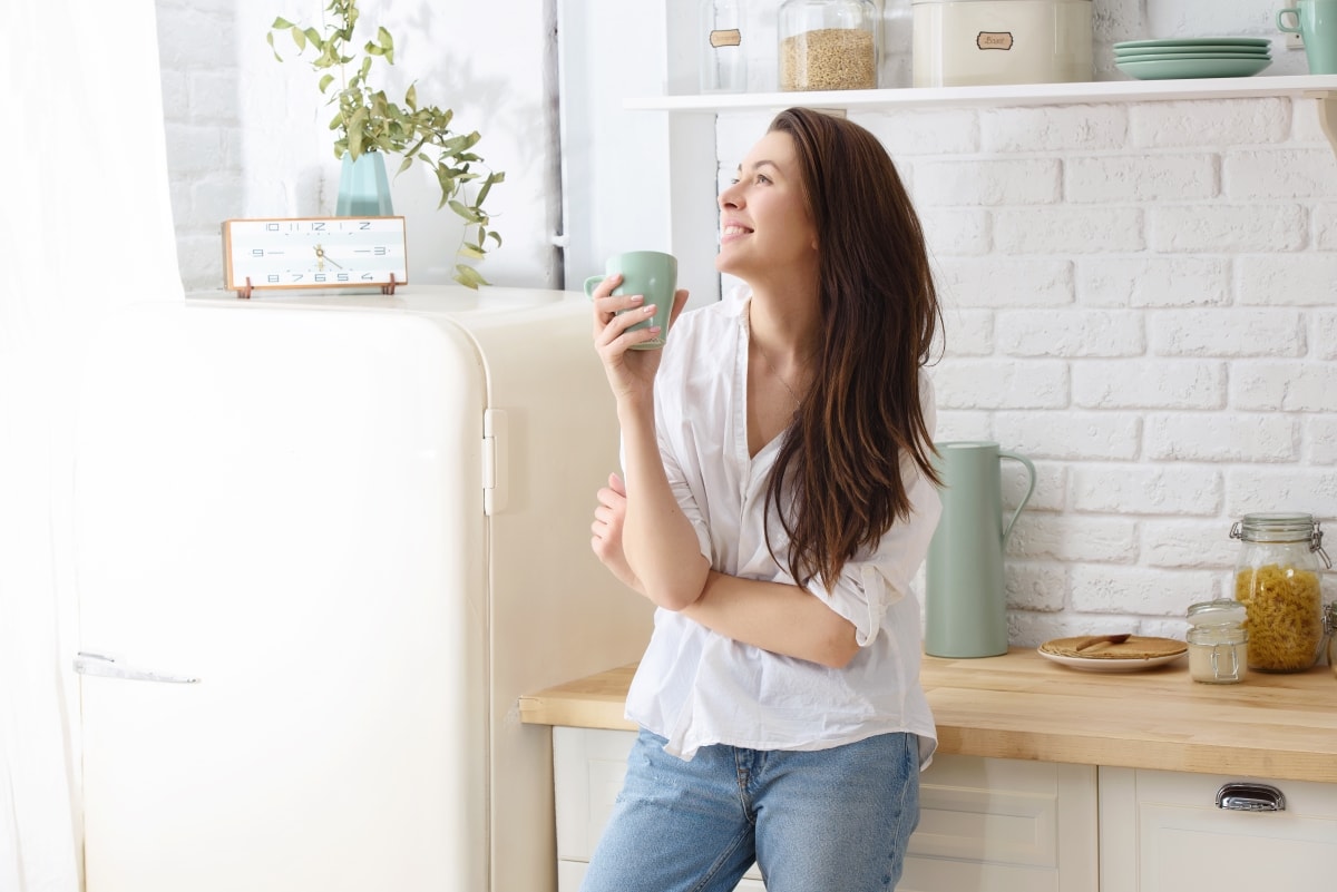 A minimalist person smiling and staring into the future, while drinking coffee in the kitchen