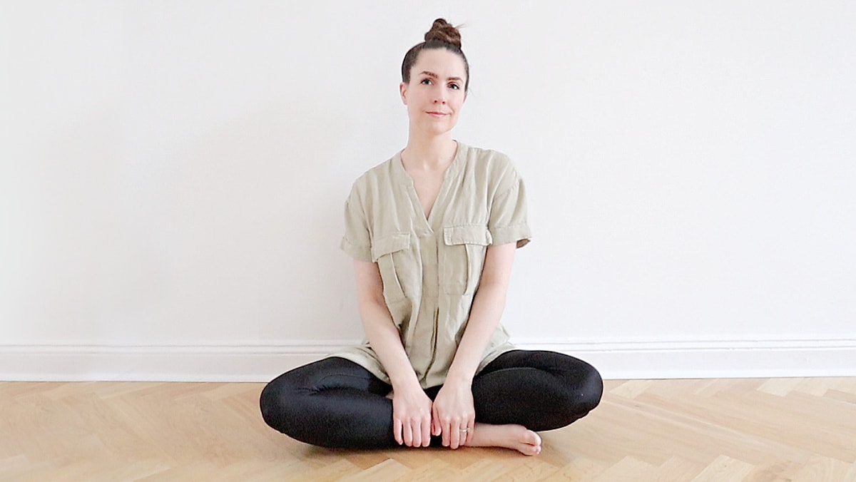 A minimalist person in neutral clothing sitting on her wood floor at home