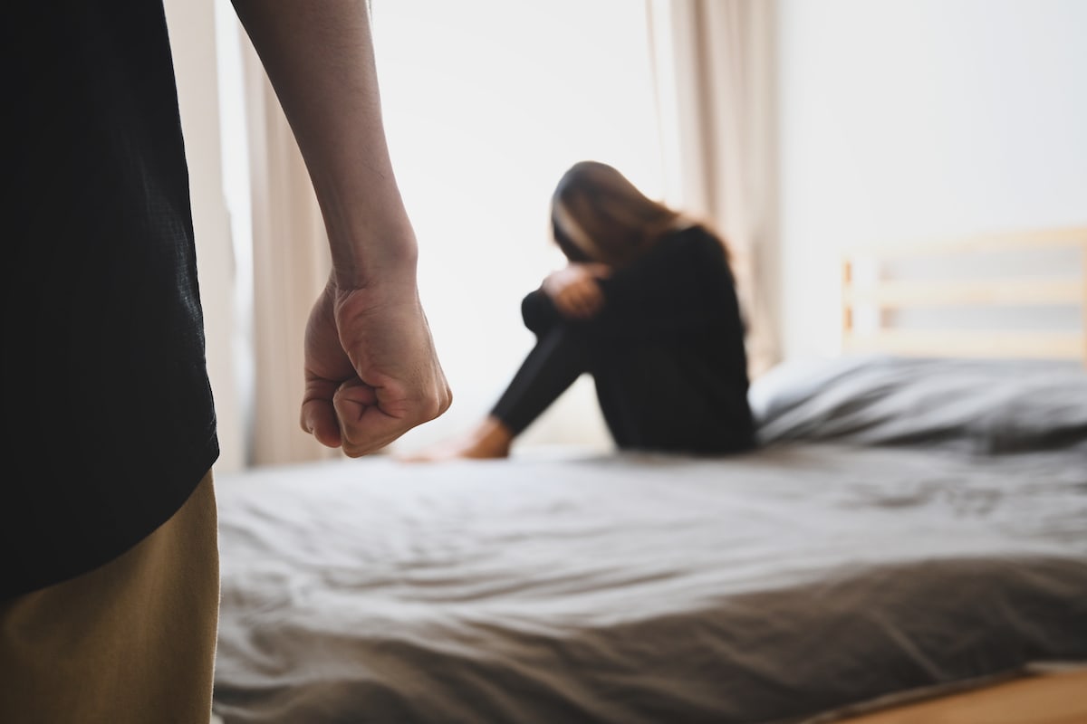 A woman in a toxic relationship cowering on a bed in front of man with clenched fist