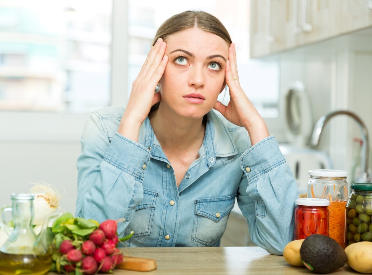 A woman experiencing buyer's remorse while sitting at her table, hands on temples.