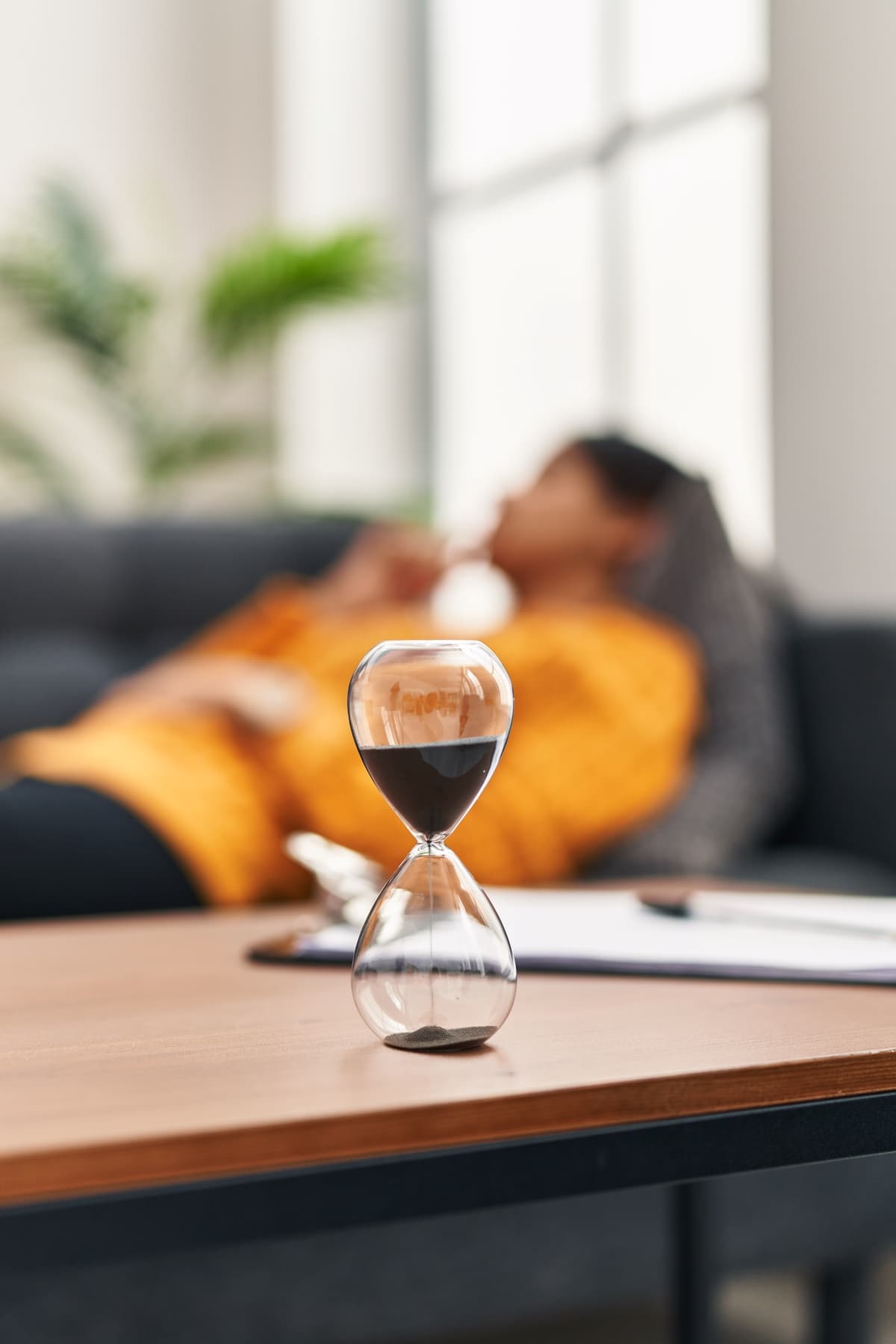 A woman on a couch talking about the value of time with her therapist, with an hourglass in the foreground