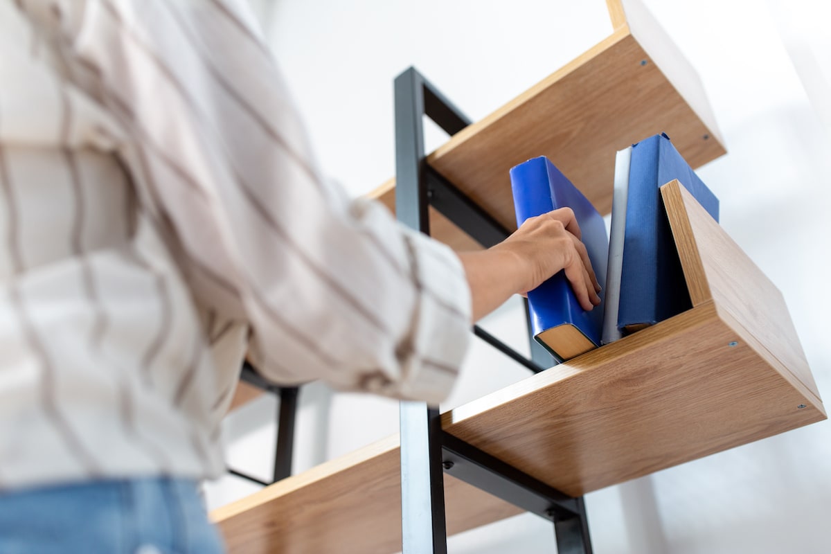 A woman pulling a book off a shelf to read the rules of decluttering.