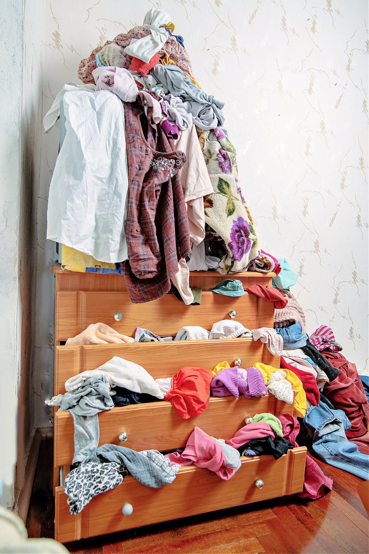 Messy dresser with too many clothes inside in the bedroom of a clothes hoarder.