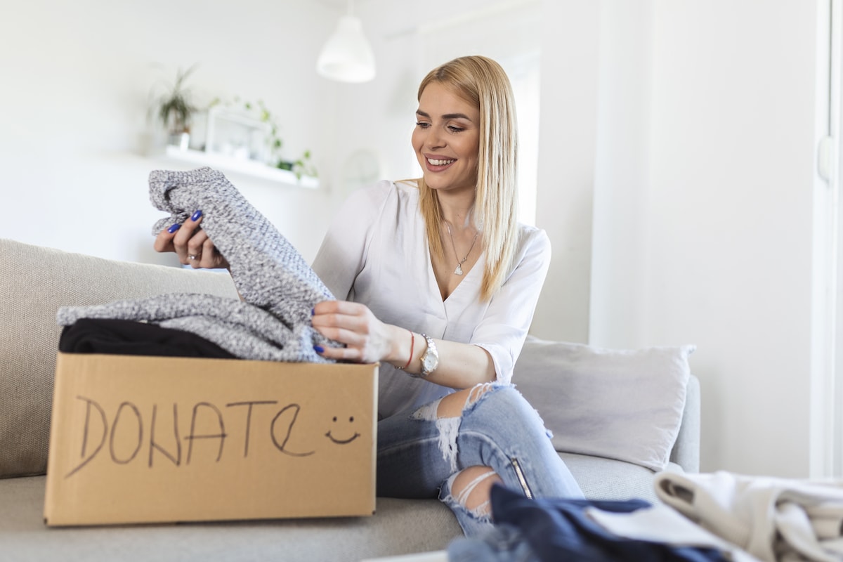 A smiling blonde woman declutter quickly and putting clothes into a box to donate
