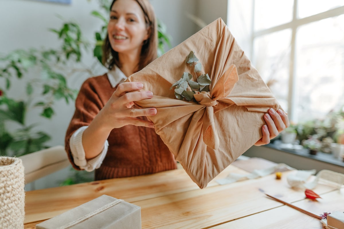 A pretty woman holding out a hand-wrapped hygge gift in natural wrapping.