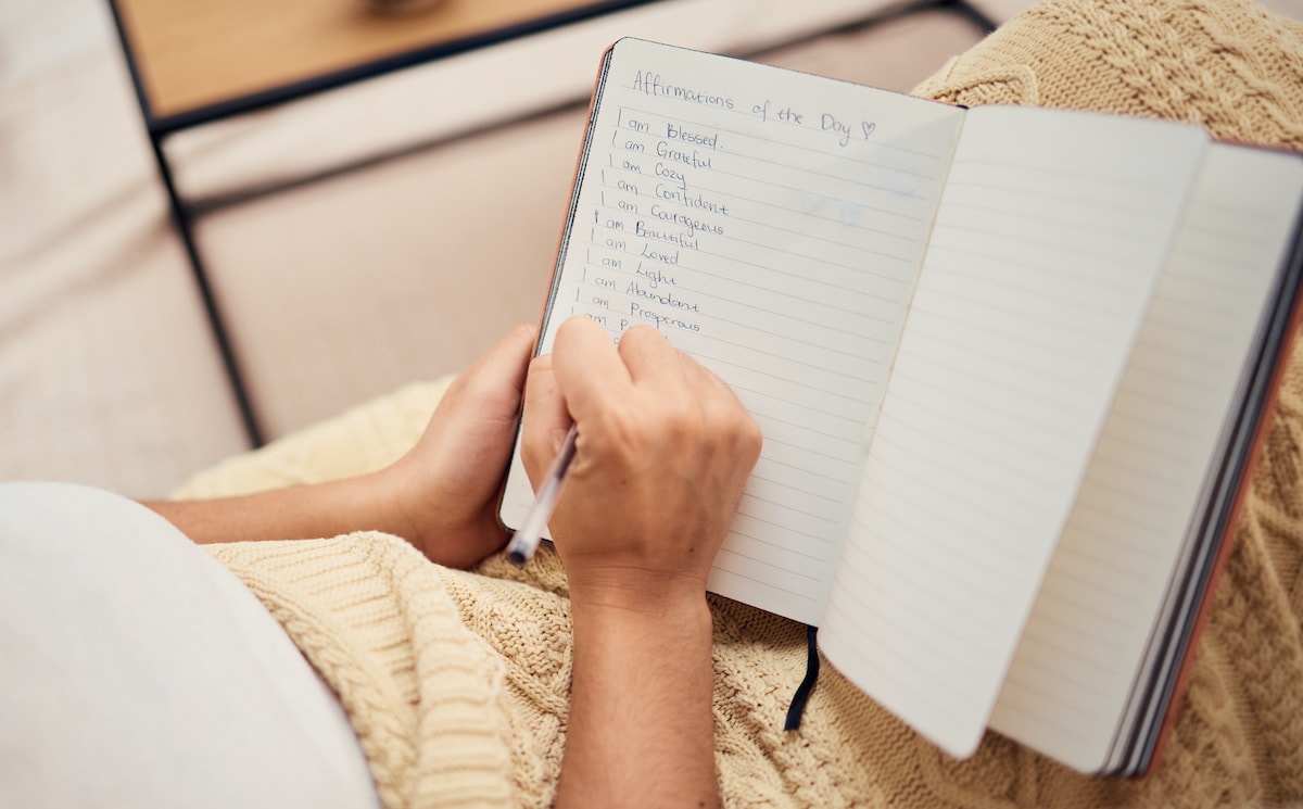 A woman writing affirmations about getting her life together in a journal