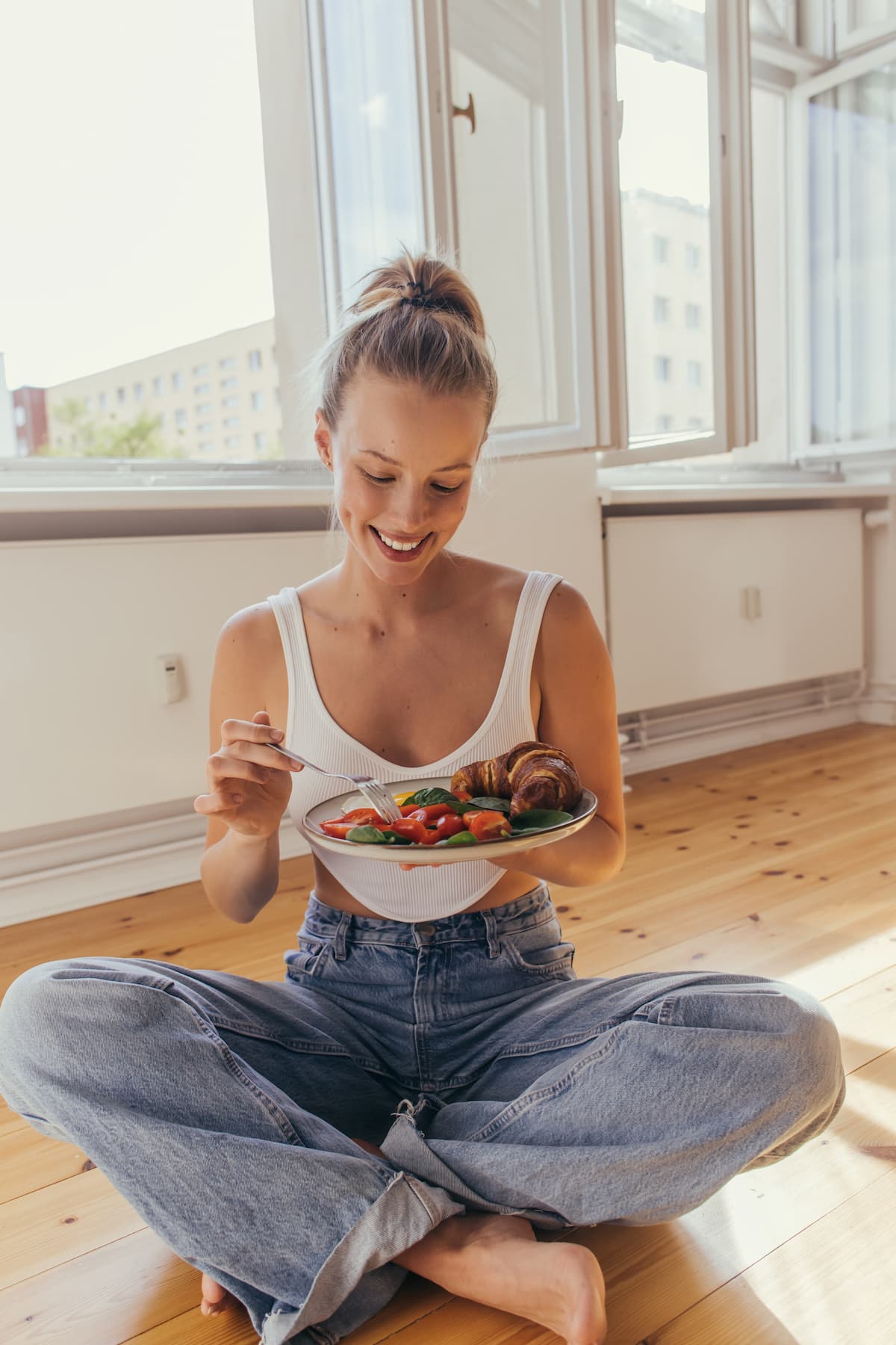 A happy woman sitting on the floor, trying to get her life together and eat better.